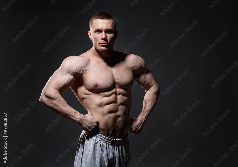 Muscular man in studio over dark background shows his body 