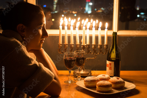 Girl sits by candles on Hanukkah holiday. Hanukkah celebration attributes. Judaic holiday of lights.