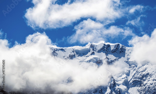 Close view of snowy mountain ridge shrouded in clouds. Blue sky. Clear summit. North Caucasus.
