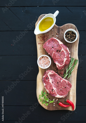 Raw fresh meat Ribeye steak entrecote and seasonings on cutting board over dark wooden background