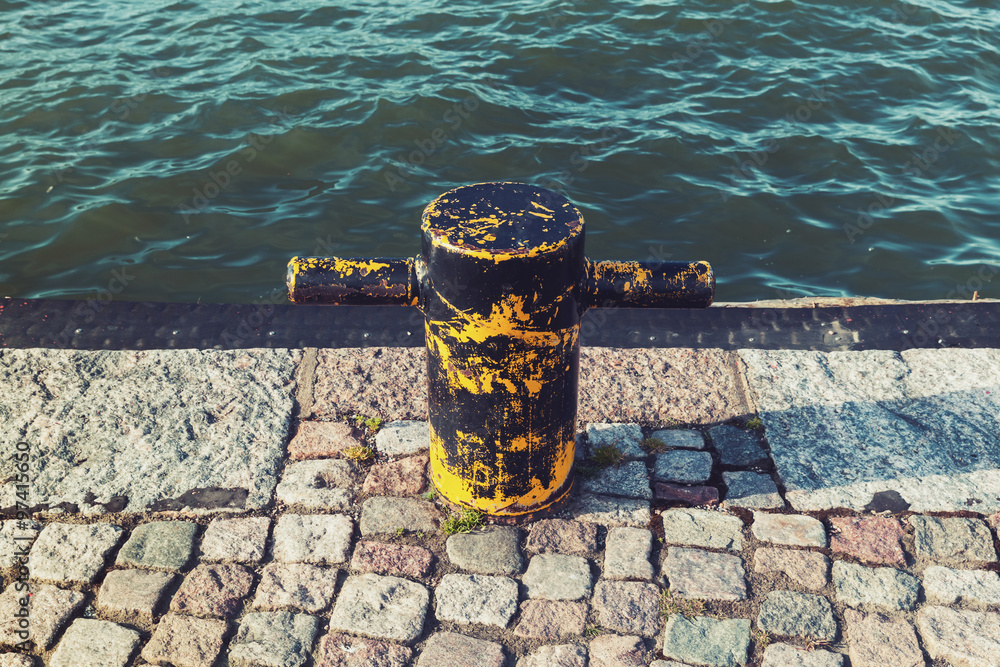 Naklejka premium Old rusted yellow mooring bollard on stone pier