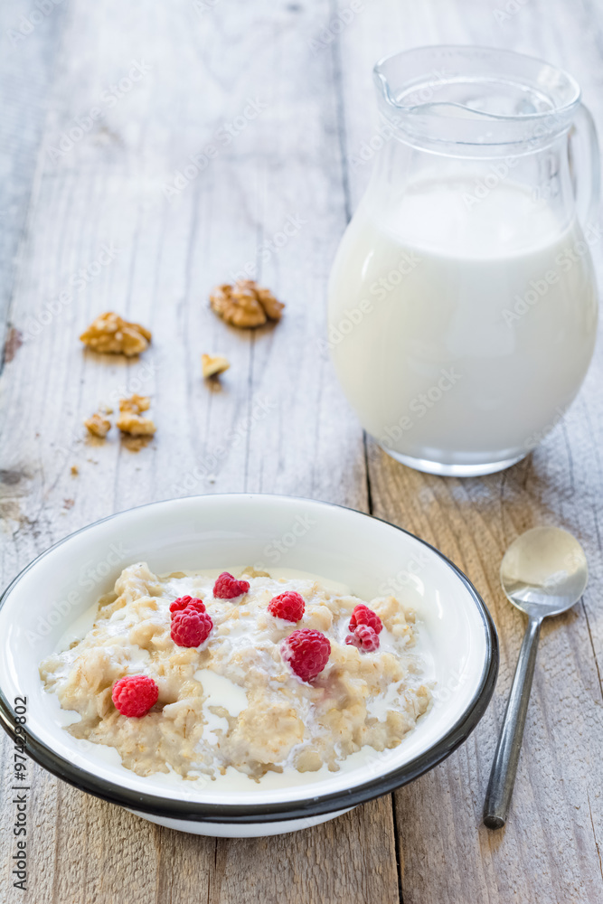 Oatmeal porridge with raspberries and milk on textured wooden table, country style healthy breakfast. Vertical composition Oatmeal porridge with raspberries and milk on textured wooden table, country style healthy breakfast. Vertical composition