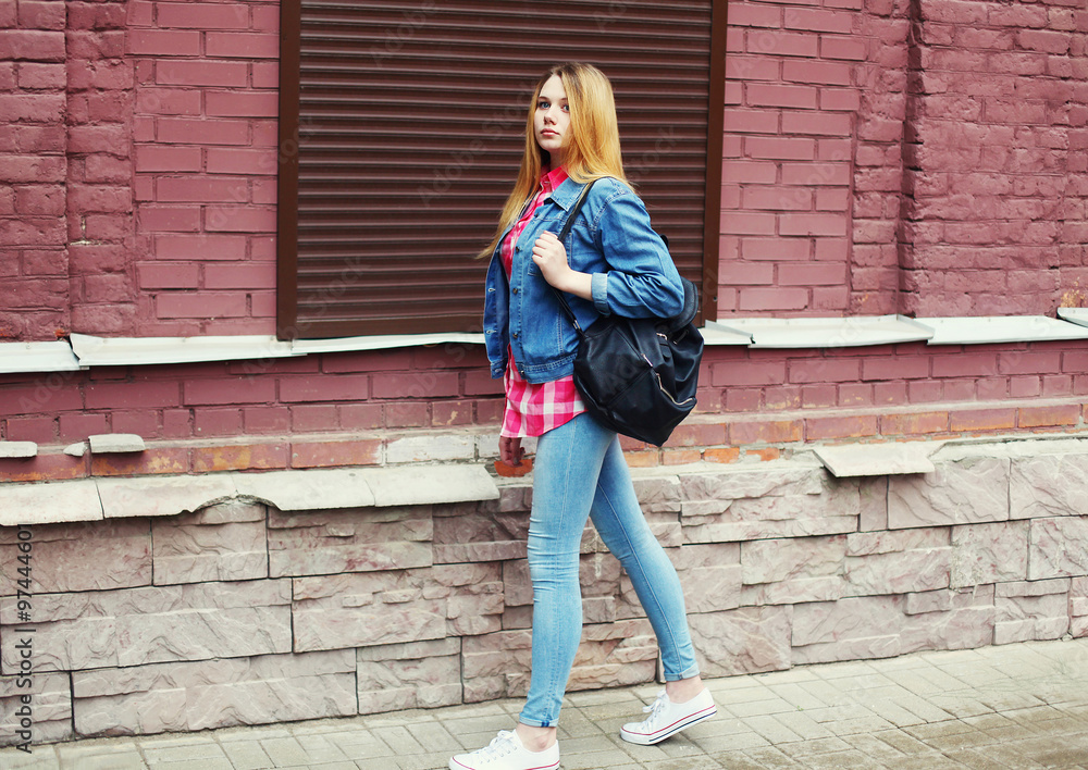 Pretty young girl wearing a jeans jacket and black bag walking i