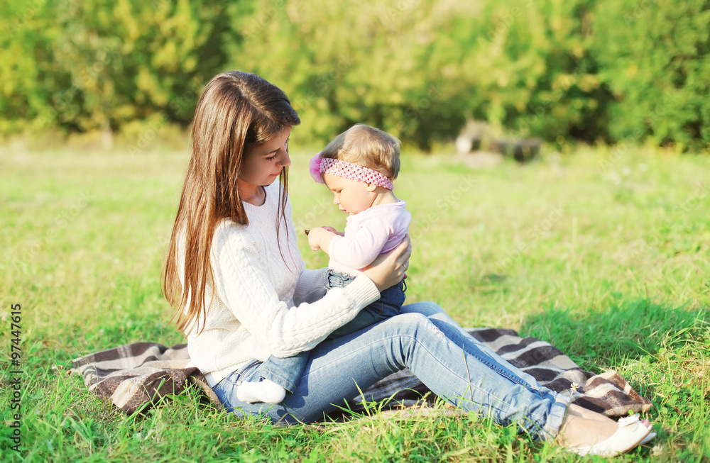 Happy mother and baby sitting together on grass in sunny day