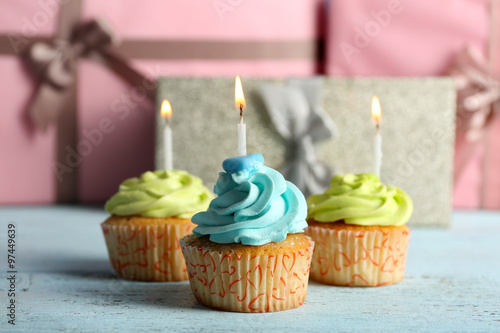 Delicious cupcakes with candles on violet table against wooden background