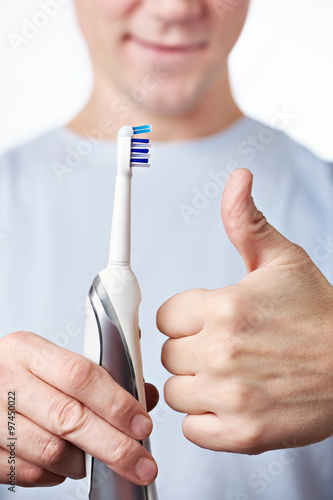 Man holding electric toothbrush and shows gesture thumbs up