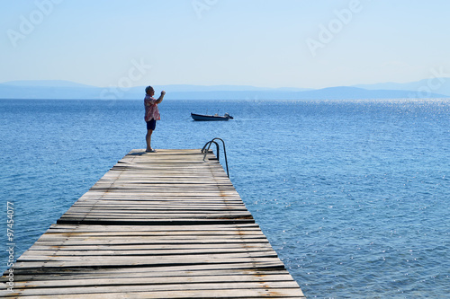 Man on an old wooden pier taking photo with his phone