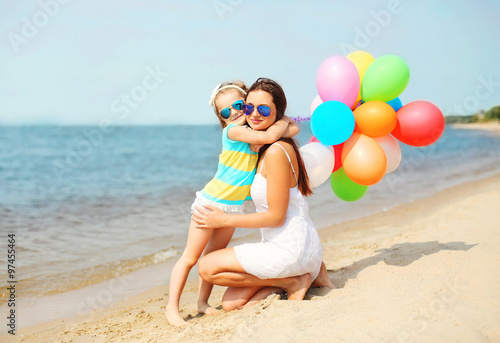 Mother and child hugging with colorful balloons on beach near se