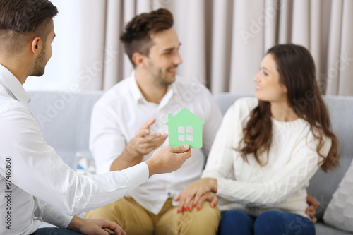 Estate agent with model of house and happy couple on home interior background