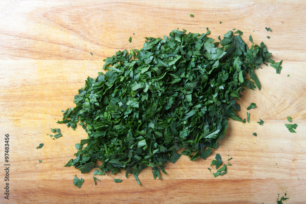 Finely chopped fresh parsley on a light wooden table or cutting Finely chopped fresh parsley on a light wooden table or cutting