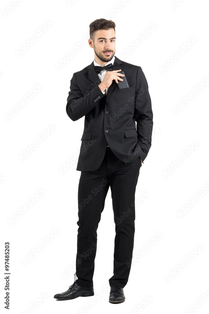 Smiling confident luxurious man in suit putting cellphone in suit pocket looking at camera. Full body length portrait isolated over white studio background. Smiling confident luxurious man in suit putting cellphone in suit pocket looking at camera. Full body length portrait isolated over white studio background.