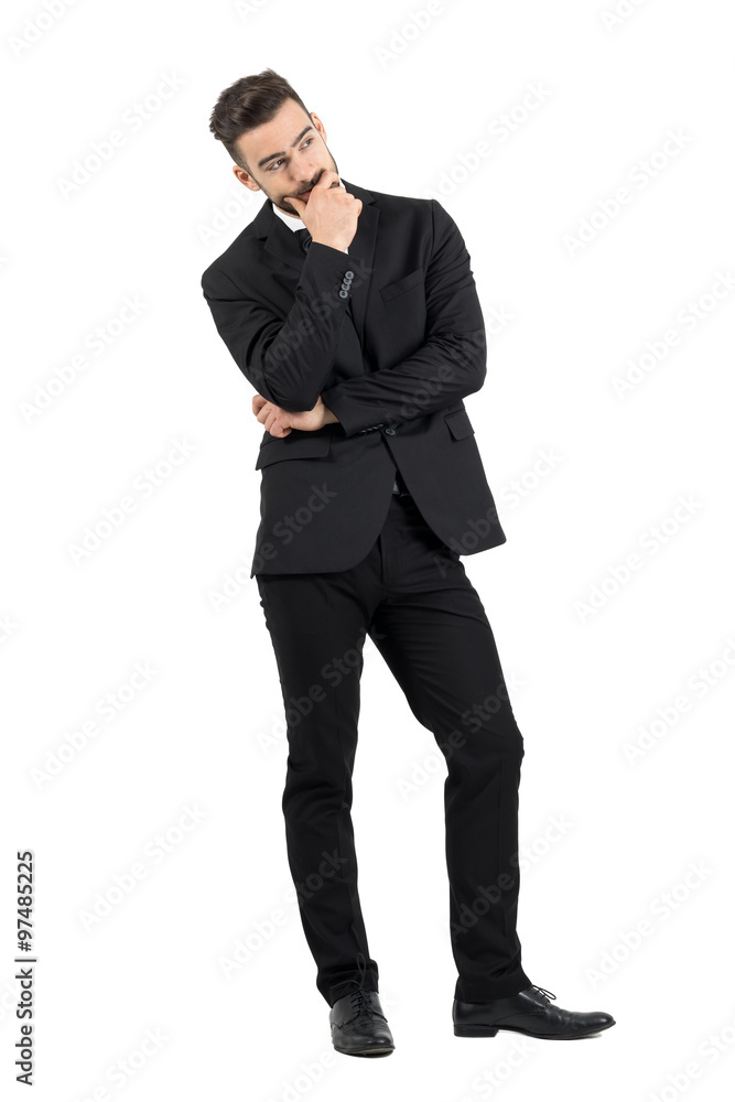 Pensive young businessman thinking with hand over his mouth looking away. Full body length portrait isolated over white studio background. Pensive young businessman thinking with hand over his mouth looking away. Full body length portrait isolated over white studio background.