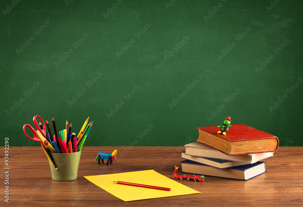 School items on desk with empty chalkboard School items on desk with empty chalkboard