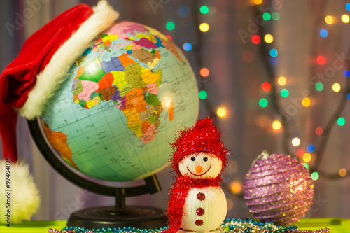 Merry Christmas Snowman on the background of the globe in a cap of Santa Claus