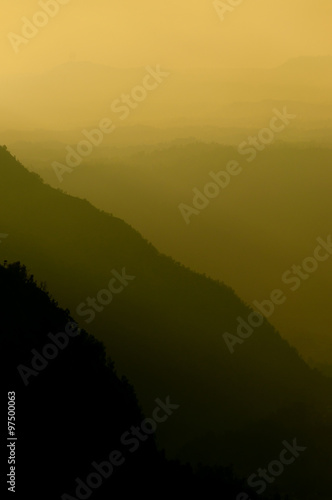 Steep black mountain silhouette in front of thick yellow Fog and smoke