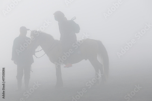 Silhouette of two person and horse in fog and smoke of volcano Bromo