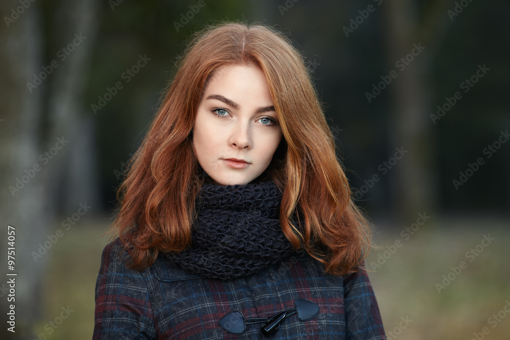 Outdoors portrait of young beautiful redhead woman in scarf and jacket on forest blurred background Outdoors portrait of young beautiful redhead woman in scarf and jacket on forest blurred background