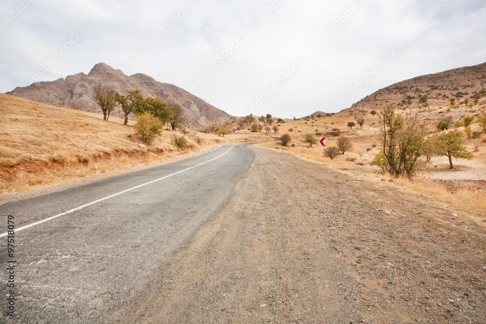 Asphalt road in a sandy valley among the mountains under clouds