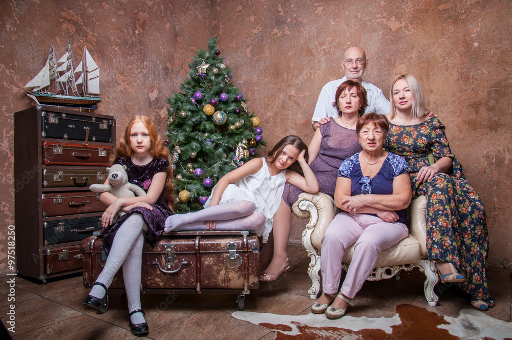 Большая семья с бабушкой, дедушкой, мамами и девочками сидят около новогодней елки