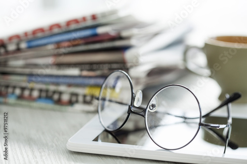 Stack of newspapers, eyeglasses and digital tablet
