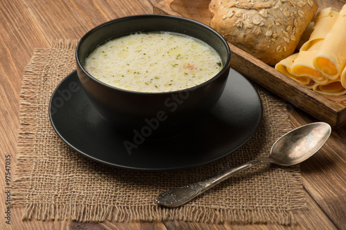 Cheese soup in a black plate on the rustic wooden background.