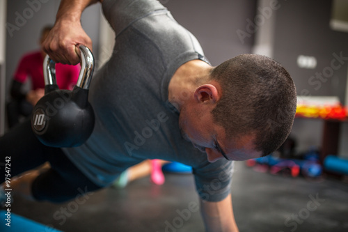 Fotografie Young man lifting dumbbell and kettlebell at the fitness center
