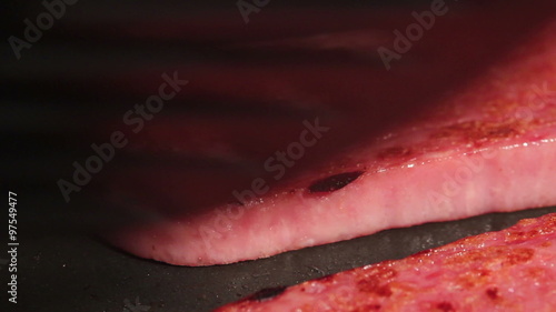 HD macro footage of a slice of canned meat product being fried in a pan, with the slice in the foreground being flipped
