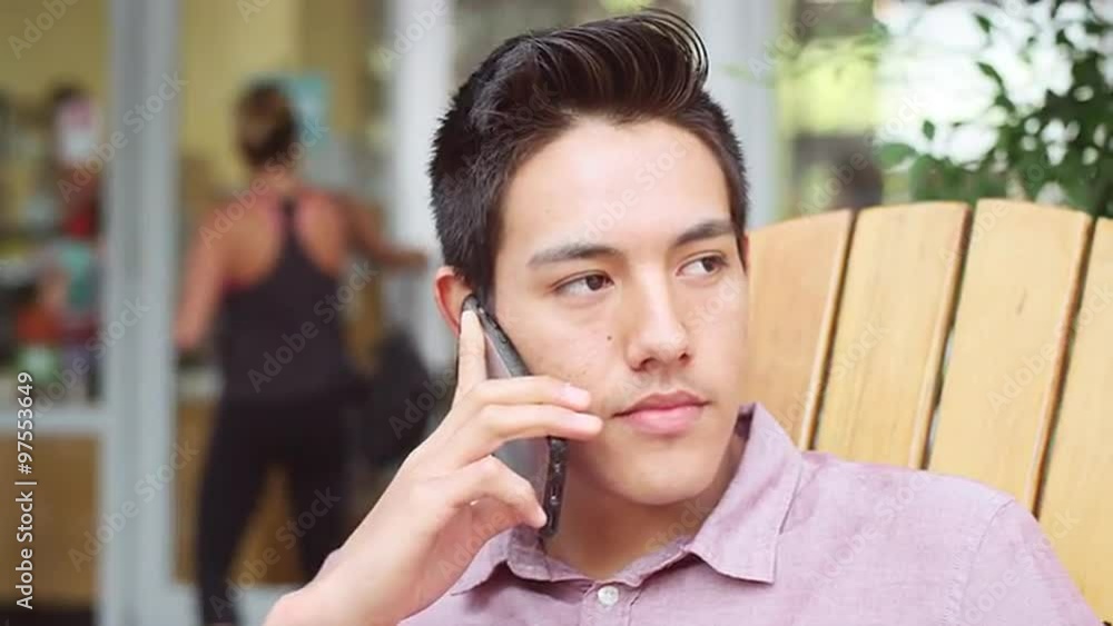 A young man sitting outside talking on his phone A young man sitting outside talking on his phone