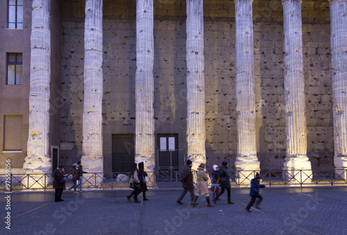 Hadrian temple colonnade in Rome at sunset light, with people walking along the street photo