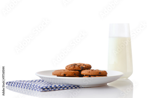 Pile of homemade chocolate chip cookies on white ceramic plate on blue napkin and glass of milk, isolated on white background