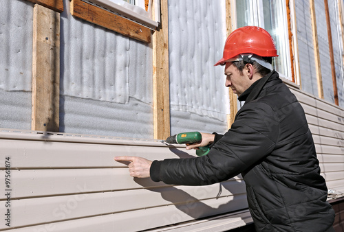 A worker installs panels beige siding on the facade