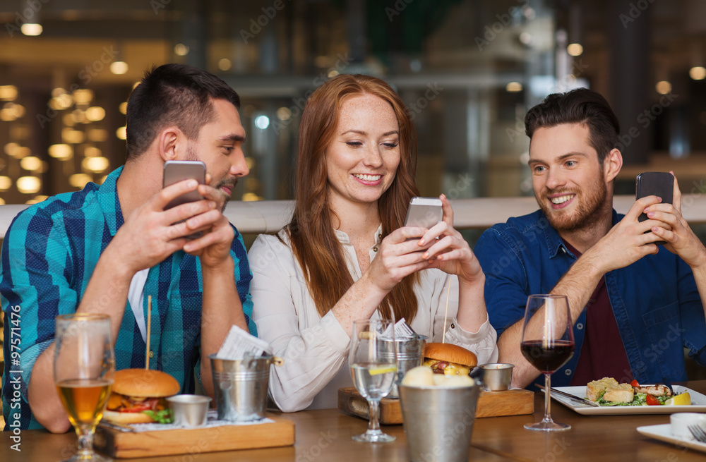 happy friends with smartphones at restaurant