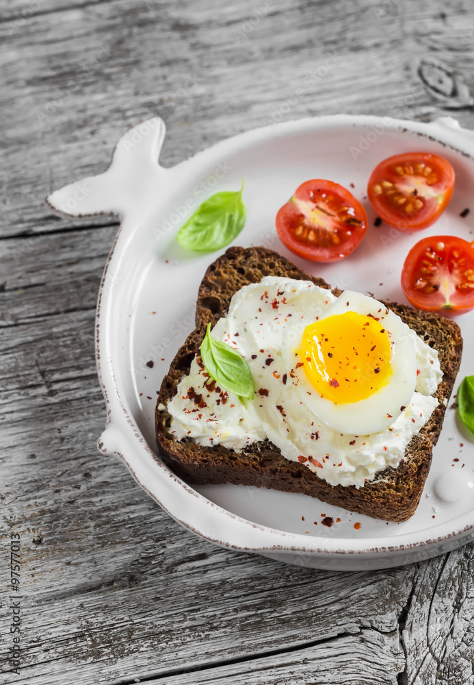 Sandwich with feta cheese and boiled egg, tomatoes, and basil on a white plate on a wooden surface. Healthy breakfast or snack