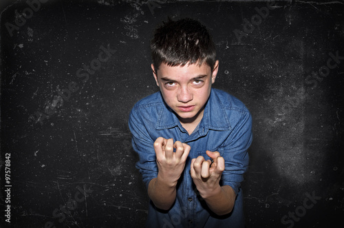 Aggressive boy. Bad caucasian teenager inviting to fight on a dark black-gray background.