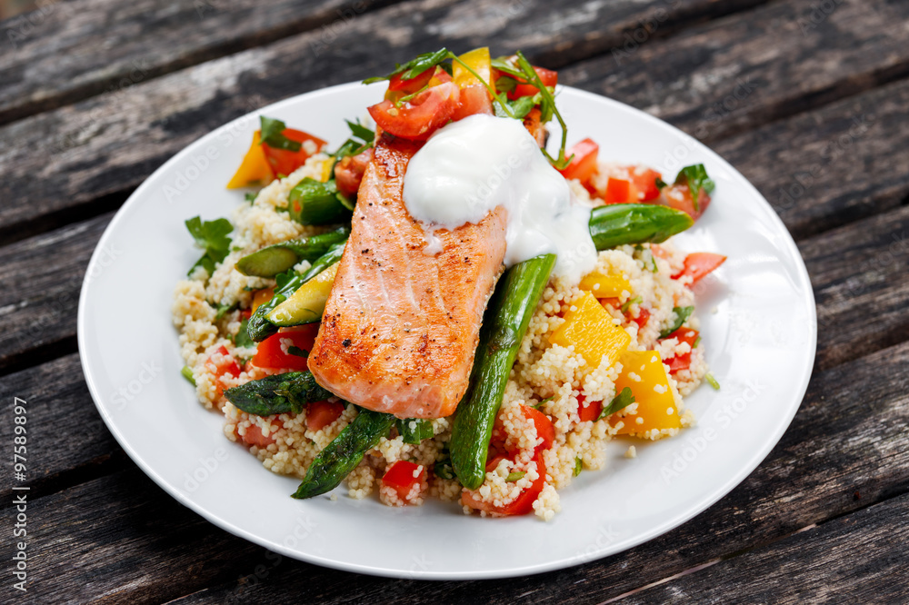Pan fried Salmon with tender asparagus, courgette served on couscous mixed with sweet tomato, yellow pepper, with greek yogurt on old wooden table. Pan fried Salmon with tender asparagus, courgette served on couscous mixed with sweet tomato, yellow pepper, with greek yogurt on old wooden table.