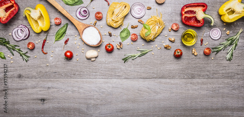 raw pasta with peppers and cherry tomatoes with a wooden spoon and salt on a long gray wooden background top view place for text,frame banner