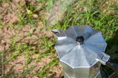 Brewing coffee with a Moka pot on a stove outdoors.