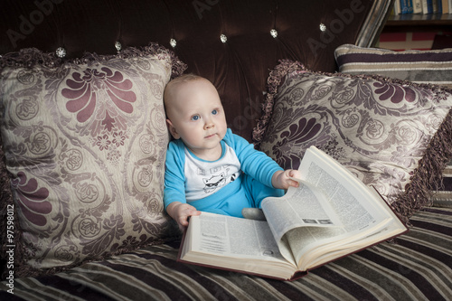Маленький мальчик с большой книжкой сидит на диване
