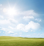 Empty field of green grass, sun light shining in blue sky