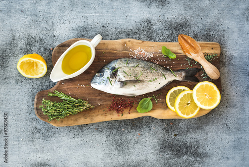 Fresh uncooked dorado or sea bream fish with lemon, herbs, oil and spices on rustic wooden board over grunge backdrop