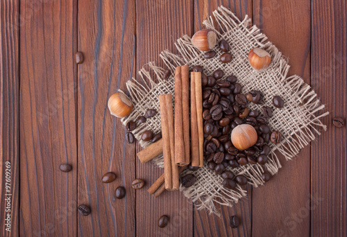 Кофейные зерна, фундук и палочки корицы на мешковине и деревянном фоне