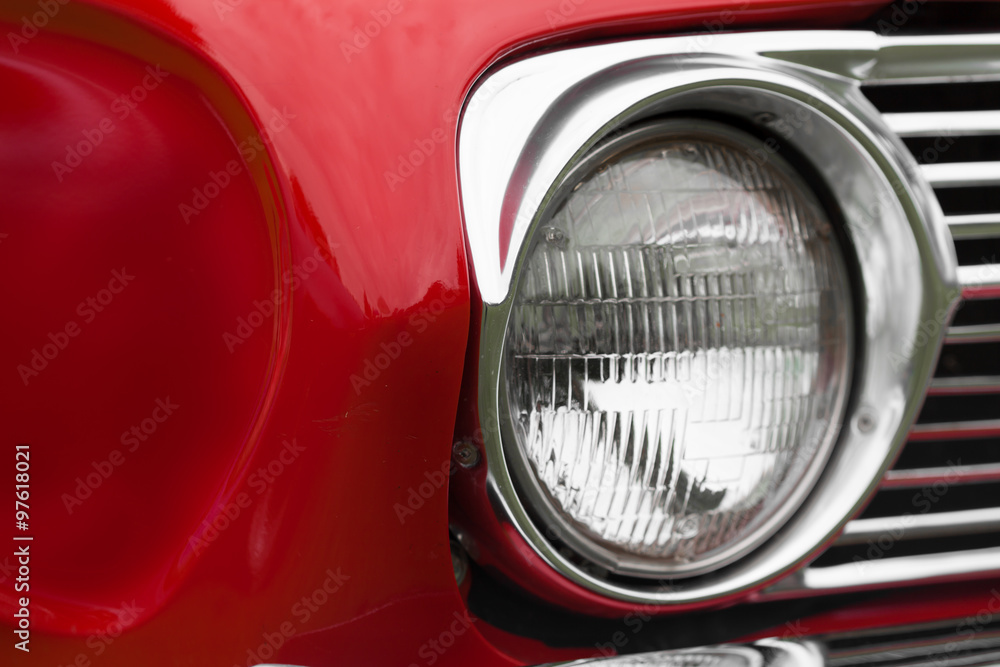Close-up of left headlight of a red shiny classic vintage car