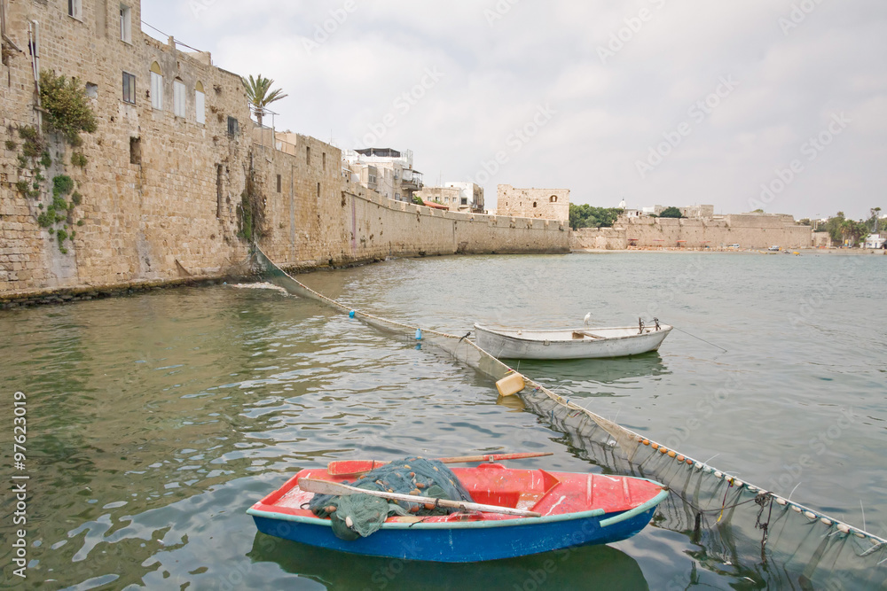 Two wooden boats moored in harbor near fishing net against sea wall background. Acre, Israel.
