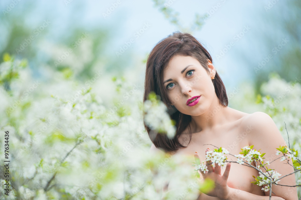 Fototapeta premium Closeup portrait of a young beautiful sexy brunette woman with white cherry flowers in bokeh background