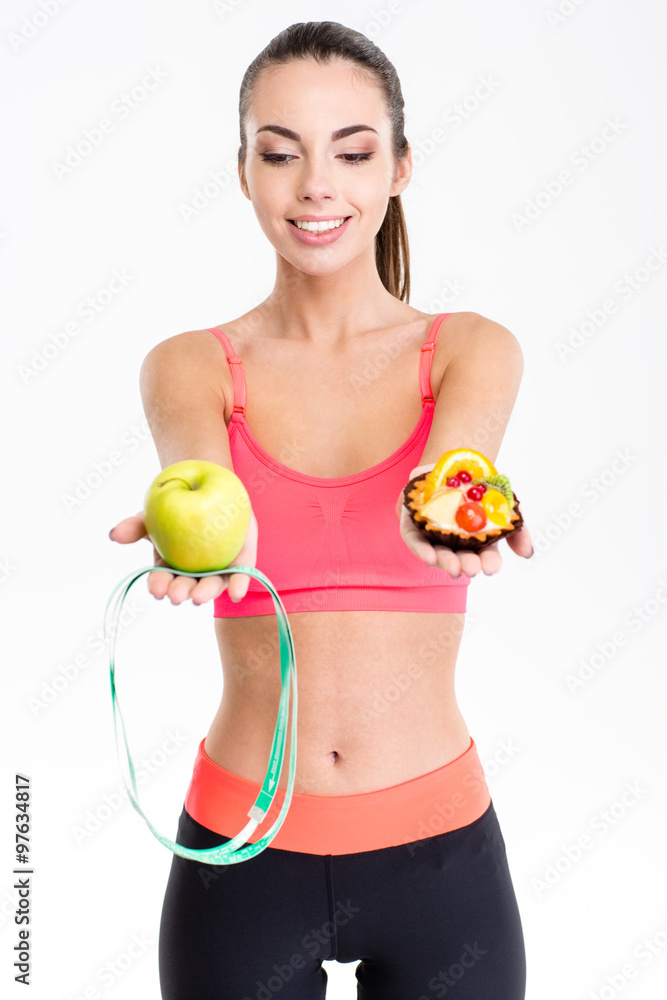 Joyful cute fitness woman making decision between apple and cake Joyful cute fitness woman making decision between apple and cake
