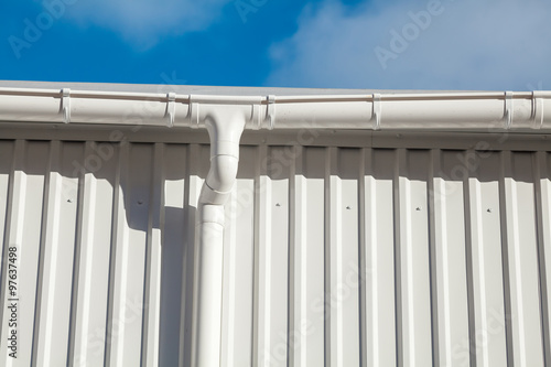 New white rain gutter on a building with white metal sheet against blue sky
