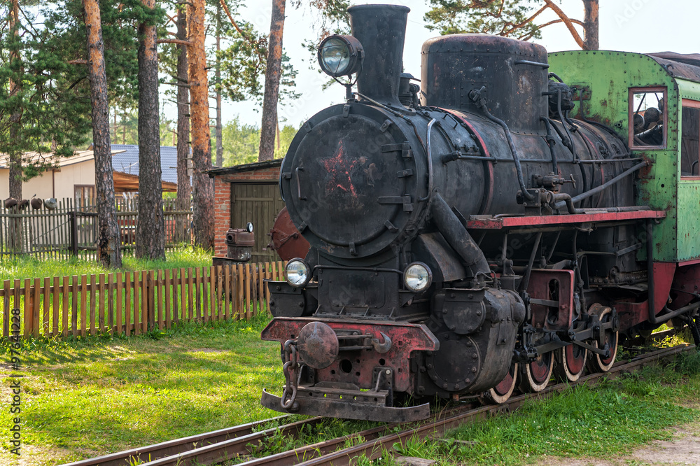 Fototapeta premium Stara czarna lokomotywa parowa stoi na zardzewiałych szynach przed ogrodzeniem. Talitsy, obwód Jarosławski, Rosja.