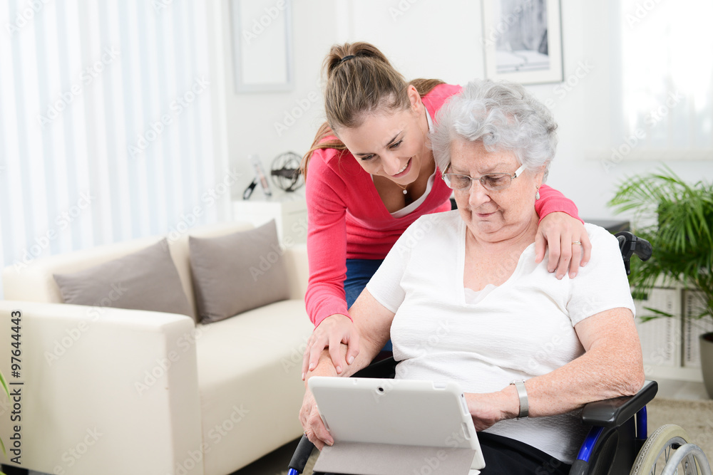 cheerful young girl teaching internet with computer tablet and sharing time with an old senior woman on wheelchair cheerful young girl teaching internet with computer tablet and sharing time with an old senior woman on wheelchair
