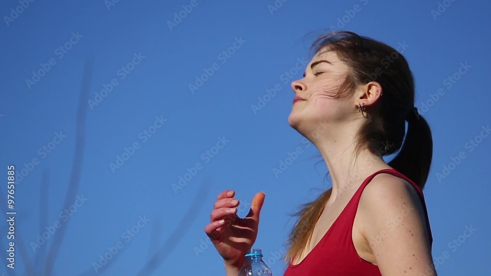 Beautiful young woman drinking from a sipping cup after workout. Shot outdoors. Blue background Beautiful young woman drinking from a sipping cup after workout. Shot outdoors. Blue background