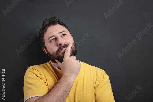 Bearded man in yellow shirt thinking in front of dark chalkboard